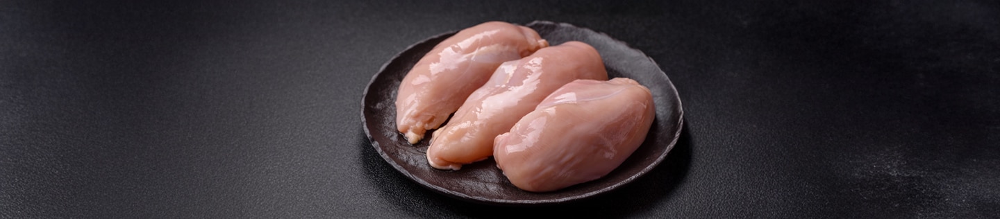 Three fresh, raw boneless chicken breast fillets arranged on a dark round plate