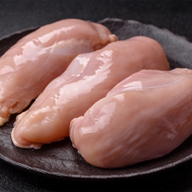 Three fresh, raw boneless chicken breast fillets arranged on a dark round plate