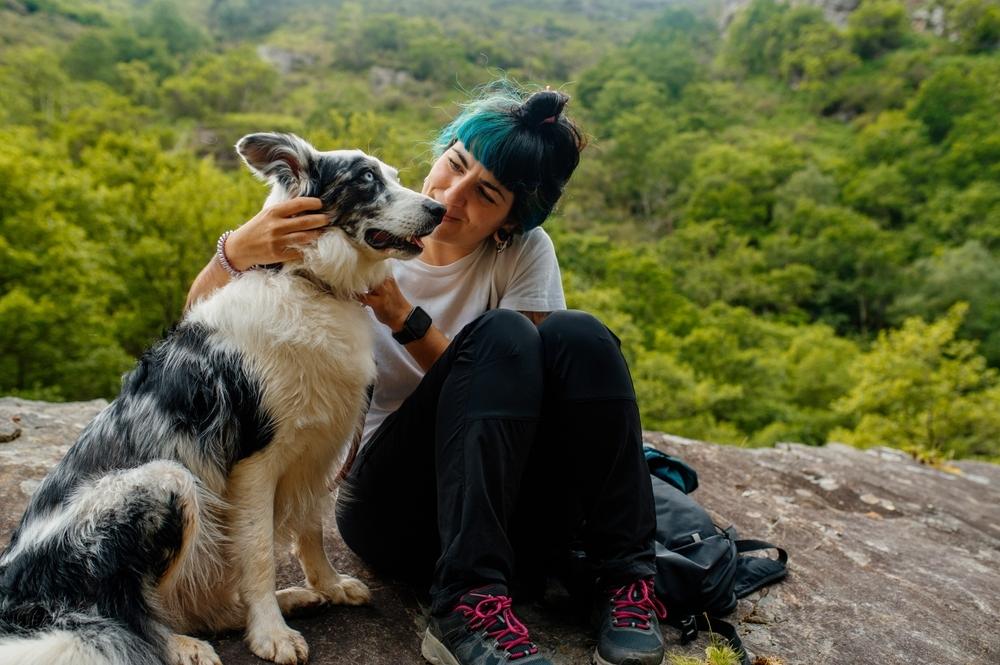 A woman and her large dog sitting on a rock