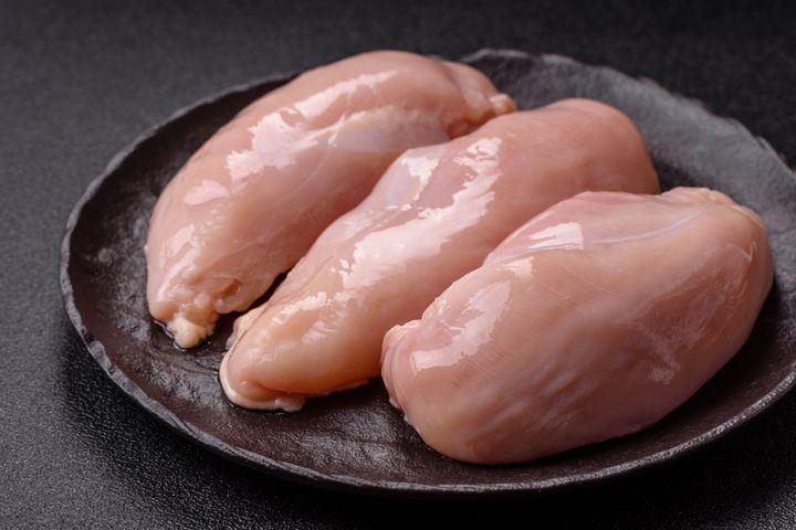 Three raw chicken breasts on a dark plate