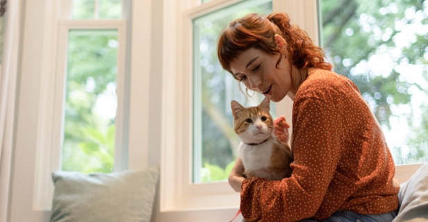 Smiling woman holding an orange and white tabby cat in front of a bright window